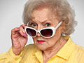 Betty White peers over white sunglasses in yellow blouse promoting AARP membership