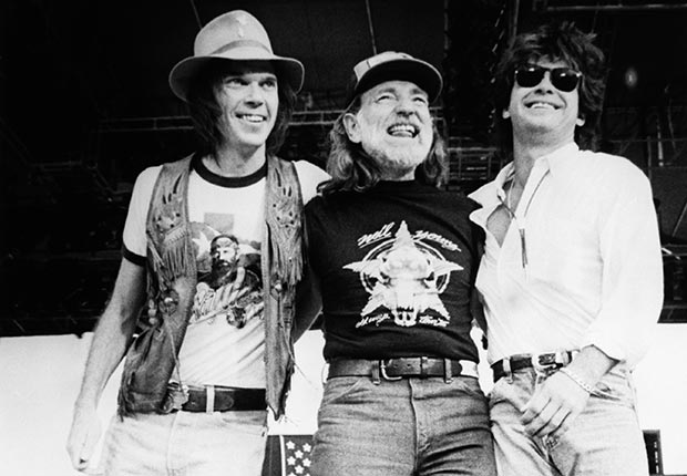Singer-songwriters Neil Young, Willie Nelson, and John Mellencamp stand together on stage during the 1985 Farm Aid Concert