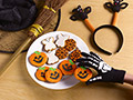 Hand wearing a skeleton glove reaches onto a plate of pumpkin and ghost shaped cookies as if stealing one from the batch, Homemade delights for Halloween