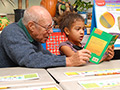 An elderly man reads to a child, AARP Experience Corps