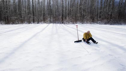 Man with snow shovel in wintery landscape-dangers of winter