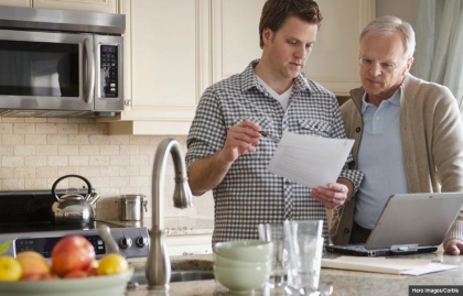 Son talking to father with paper and laptop in kitchen, Health care planning