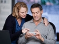 Couple operates cell phone with laptop on desk, Samsung article Innovation50+