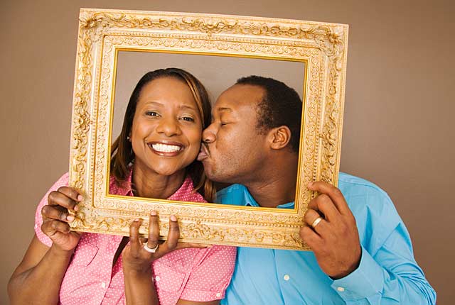 Couple kisses behind picture frame, frugal holiday season