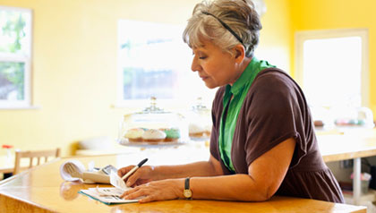 A woman pays bills at her kitchen counter