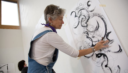 A woman creates repetitive shapes on a piece of paper.