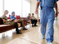 people in waiting area of hospital with a surgeon walking by