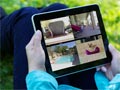 A woman outside, holding an iPad on her lap while showing house security camera images