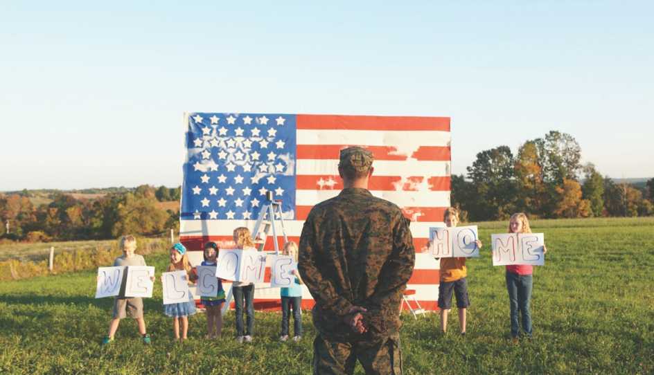 people hold up a welcome home sign as someone from the military stands before an american flag.