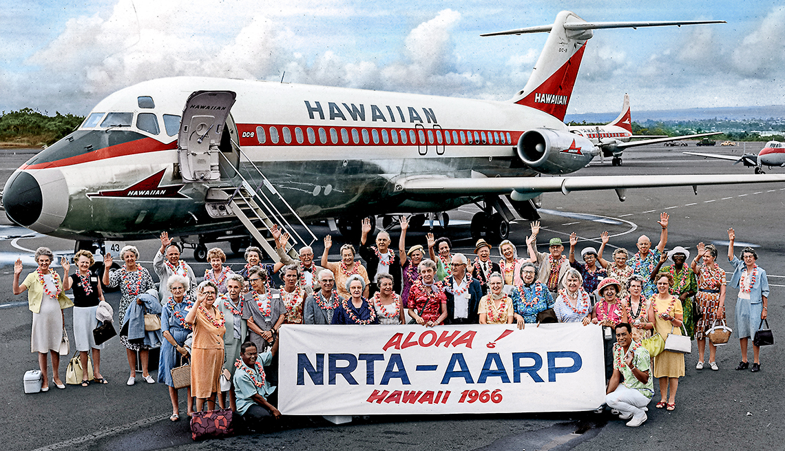 A group of people standing outside a Hawaiian plane with banner reading "Aloha! NRTA-AARP Hawaii 1966.