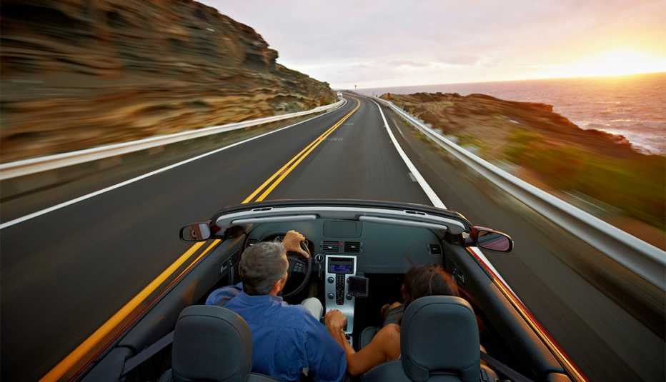 Husband and wife driving convertible along coastal road at sunrise