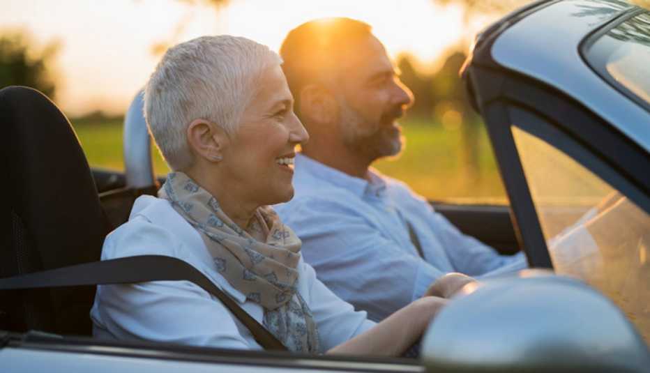 a man and a woman sitting side by side in a convertible at sundown