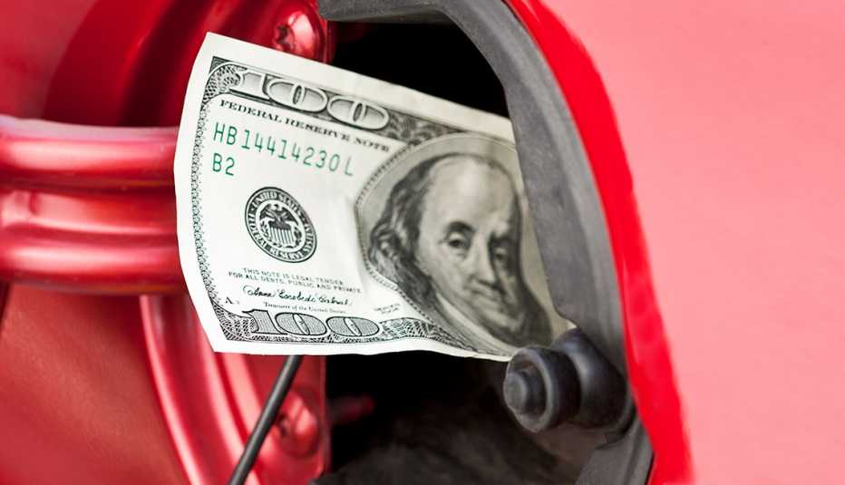 red car gas tank open with a hundred dollar bill sticking out of the fuel opening