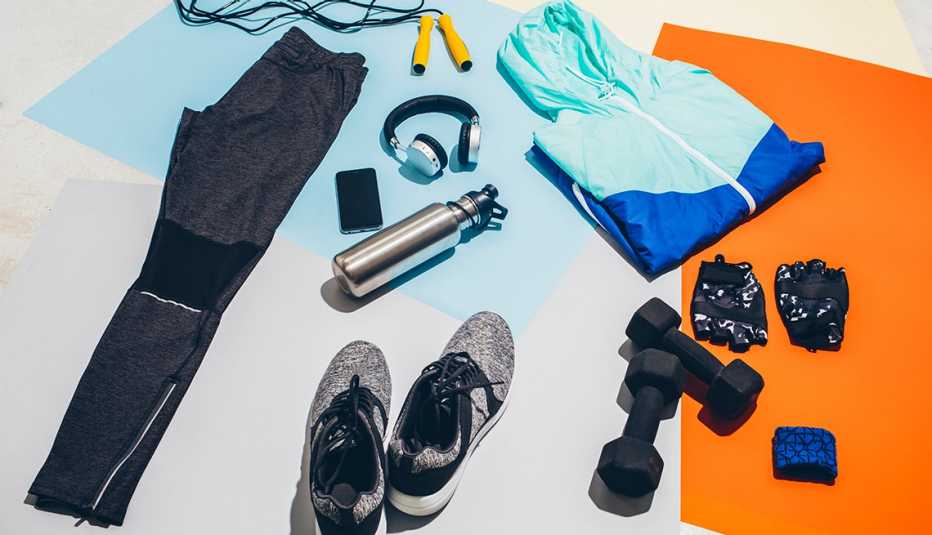 workout outfit and accessories such as hang weights headphones and water bottle are spread out on the floor atop yoga mats