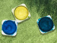 Small tubs of blue and yellow paint on green background