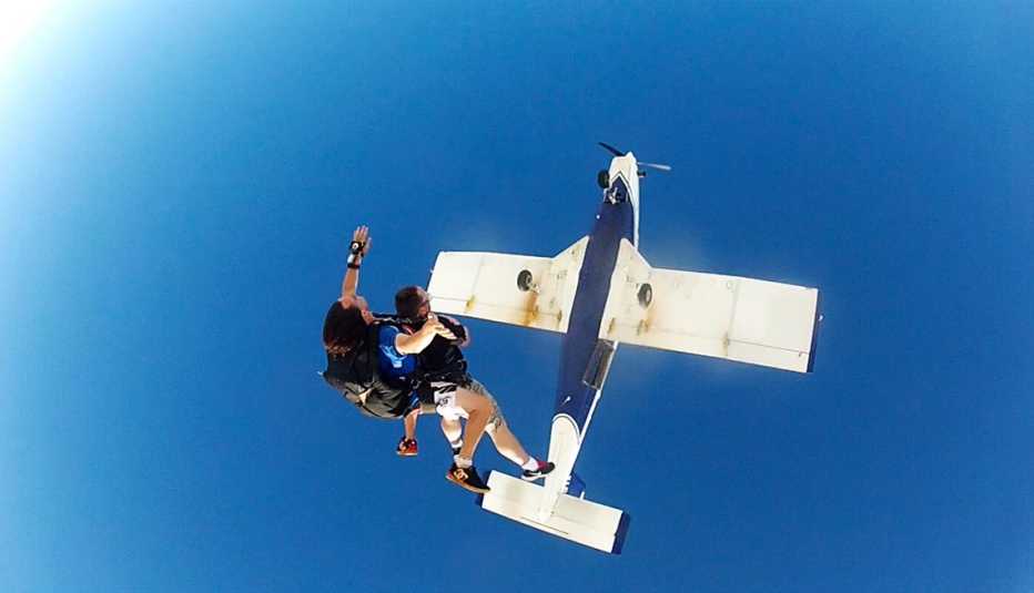 Two skydivers fall from a white propeller plane against a blue sky