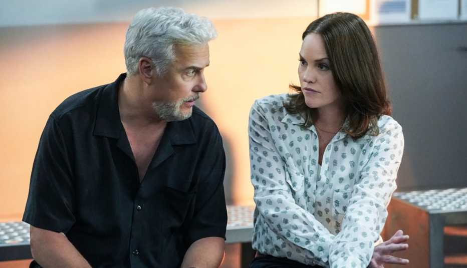 CSI's William Petersen and Jorja Fox seated and looking at each other with serious expressions