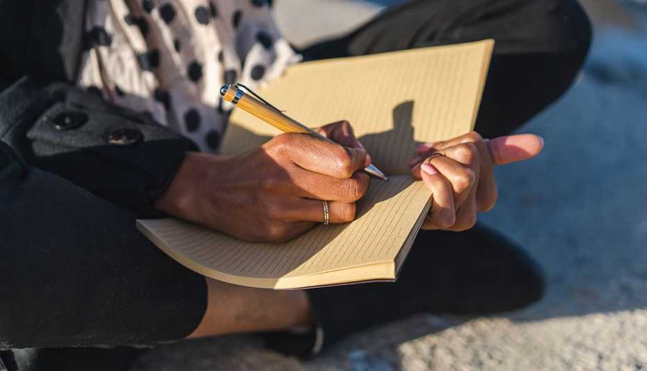 person sitting cross-legged on the ground about to write in a lined journal