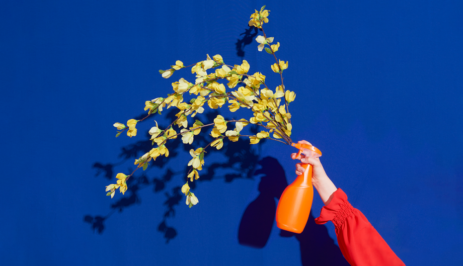 hand holding a spray bottle that appears to be spraying out flowers; blue background