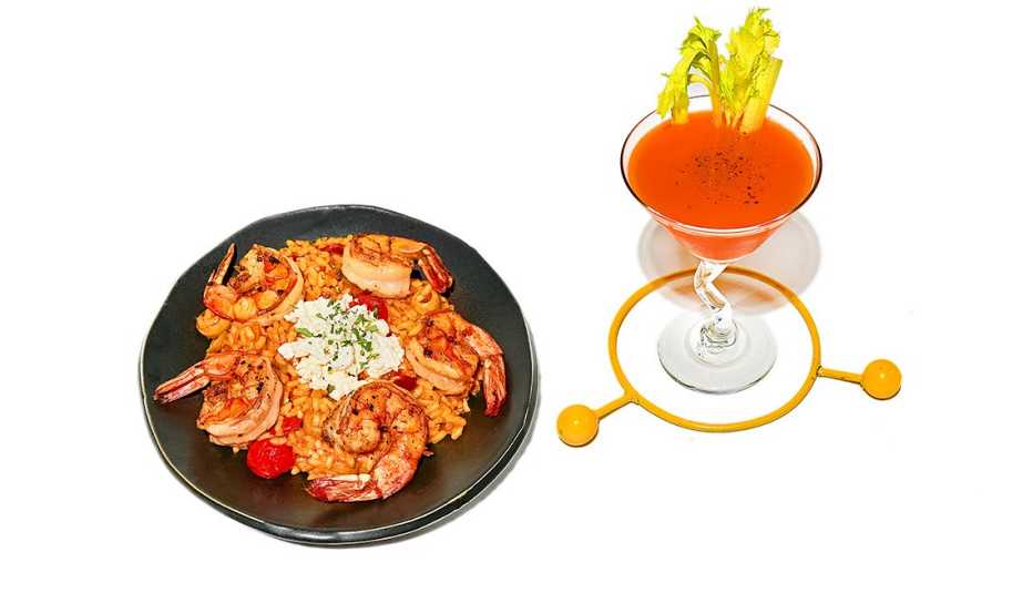 cocktail-style shrimp and mediterranean orzo on a black plate beside a glass of bloody martini 