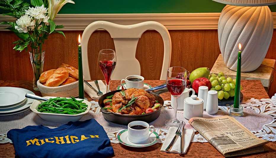 skillet roast chicken on a table with green beans, glass of wine, two cups of coffee, newspaper, tall candles, bowl of fruit, flowers, salt, pepper, sugar, and a Michigan shirt