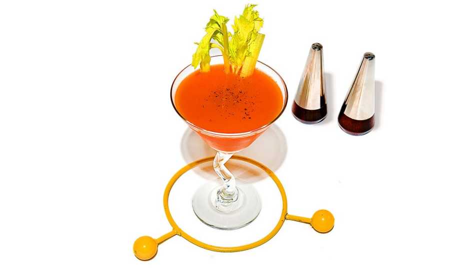 bloody martini in a glass with celery garnish standing in a yellow plastic ring beside silver conical salt and pepper shakers