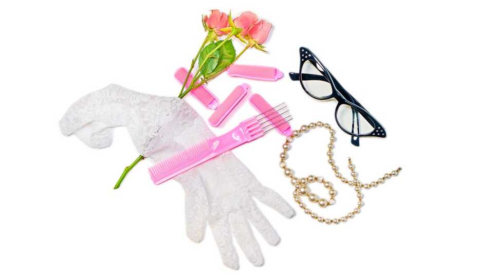 white lace glove, pink roses, pink curlers and comb, string of gold beads, black cat eye glasses