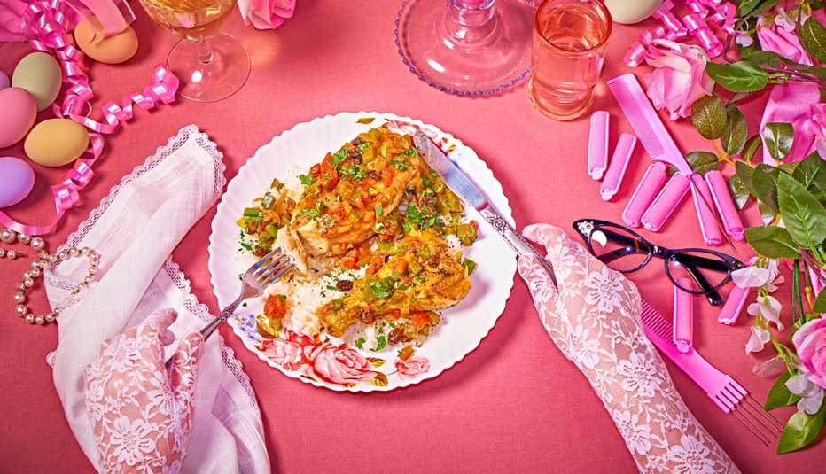 lace gloved hands holding a knife and fork over a partially eaten plate of chicken country captain on a pink table with a lace napkin, pastel eggs, black cat eye glasses, pink ribbon, curlers and combs, and more