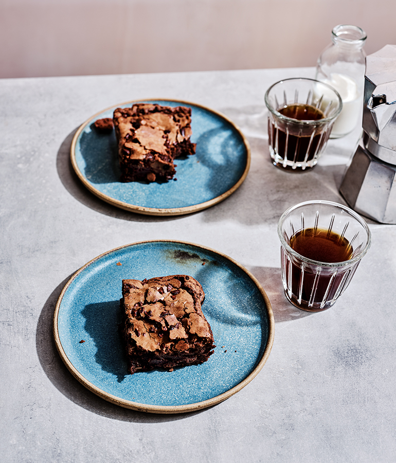 Two chocolate brownies on plates, two small glasses on coffee
