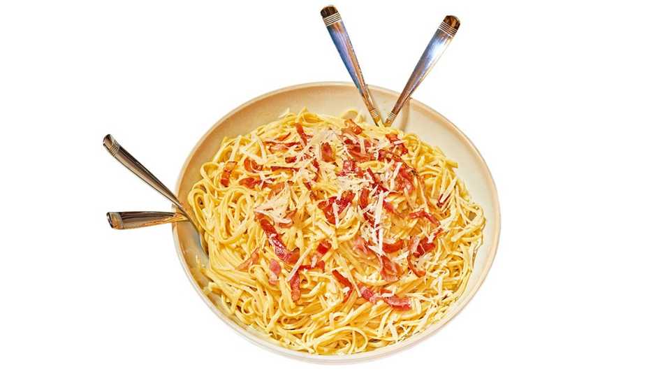 bowl of spaghetti carbonara with four utensil handles sticking out