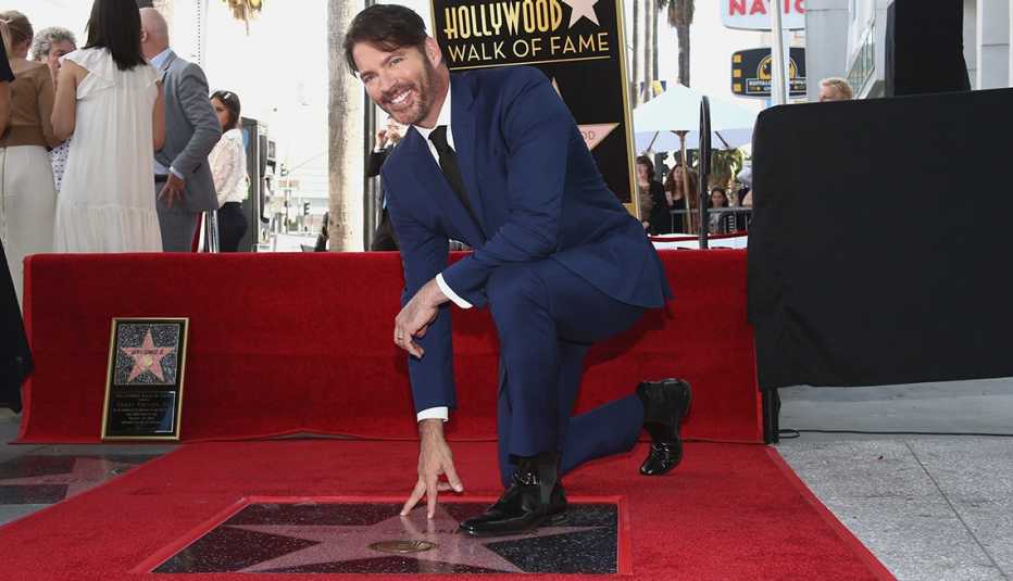 harry connick junior kneeling on his hollywood walk of fame star, touching it with one hand; people in background