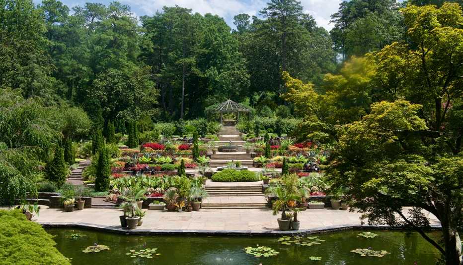 large garden with various types of flowers and trees lining concrete steps; water in front