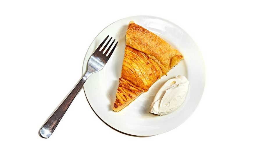 slice of pear galette with a dollop of whipped cream on a plate beside a fork