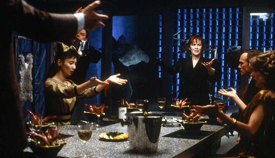 Beetlejuice dinner scene with Jeffrey Jones (hands, foreground), Adelle Lutz, Glenn Shadix, Catherine O'Hara, Dick Cavett, Susan Kellermann with their palms in the air gathered around a table set with shrimp cocktail dishes and glasses of white wine