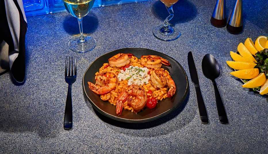 cocktail-style shrimp and mediterranean orzo on a black plate beside a plate of lemon slices