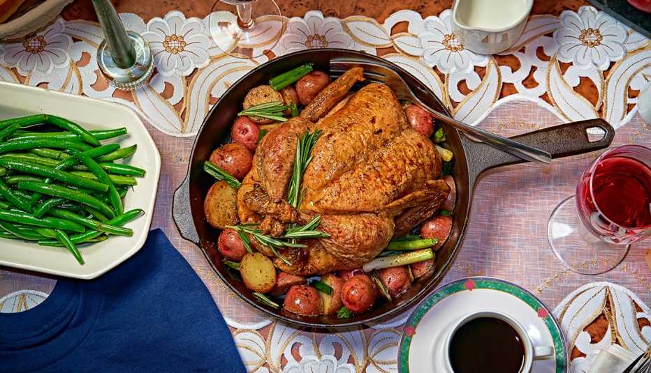 overhead shot of roast chicken in a skillet with potatoes and spring onions, a platter of green beans, cup of coffee and glass of wine
