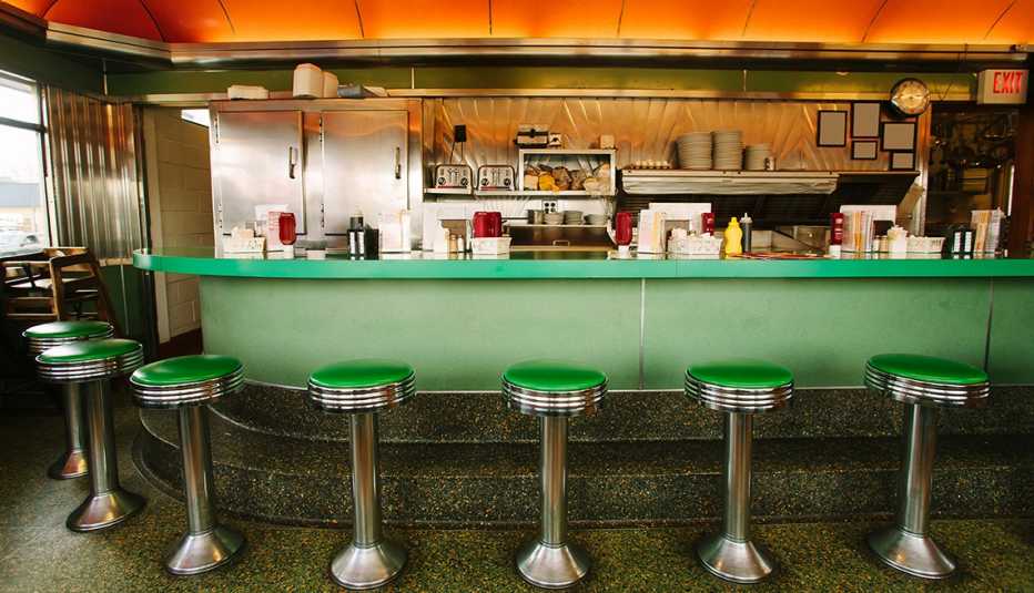 green counter in restaurant with stools in front of it; condiments and napkins on counter; restaurant supplies behind it