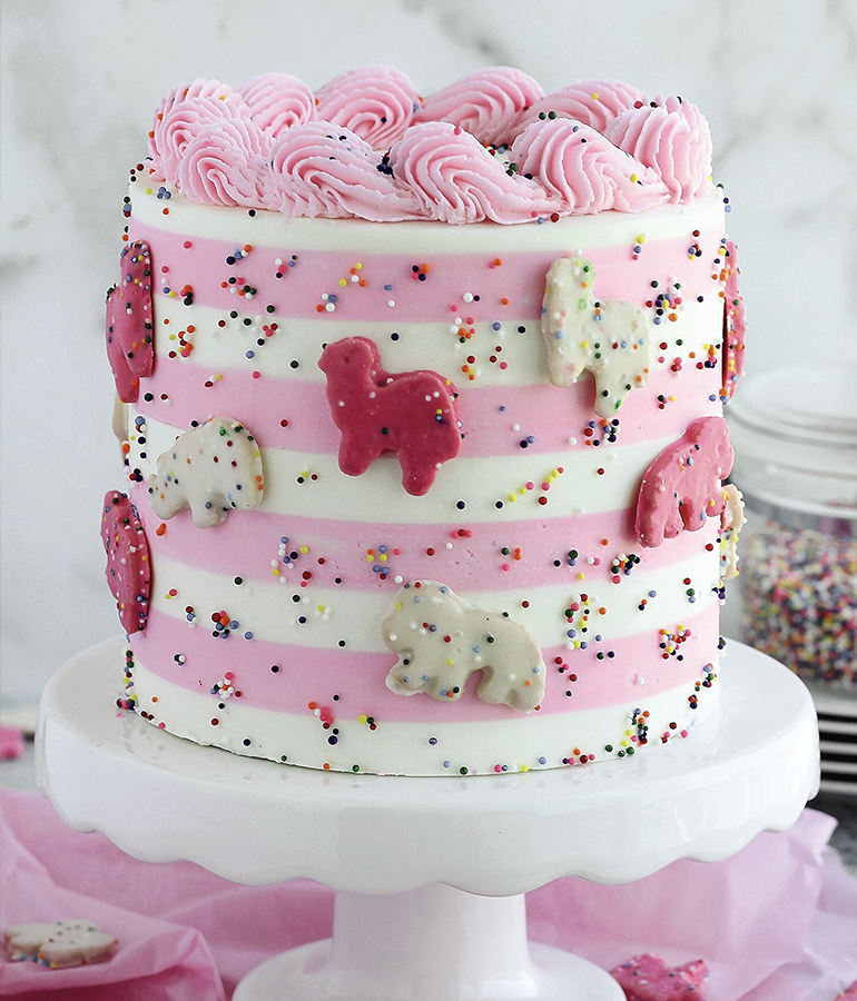 pink and white cake with pink and white animal cookies on outside on cake stand