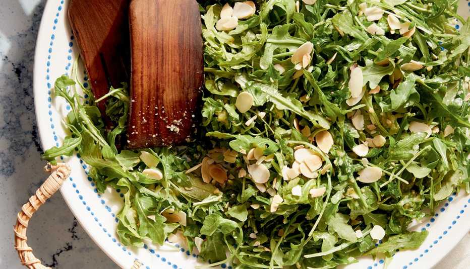 salad with arugula and sliced almonds in bowl with wooden tongs