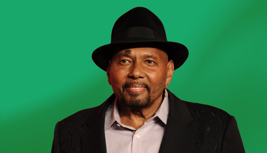 aaron neville wearing black hat and suit jacket against green background