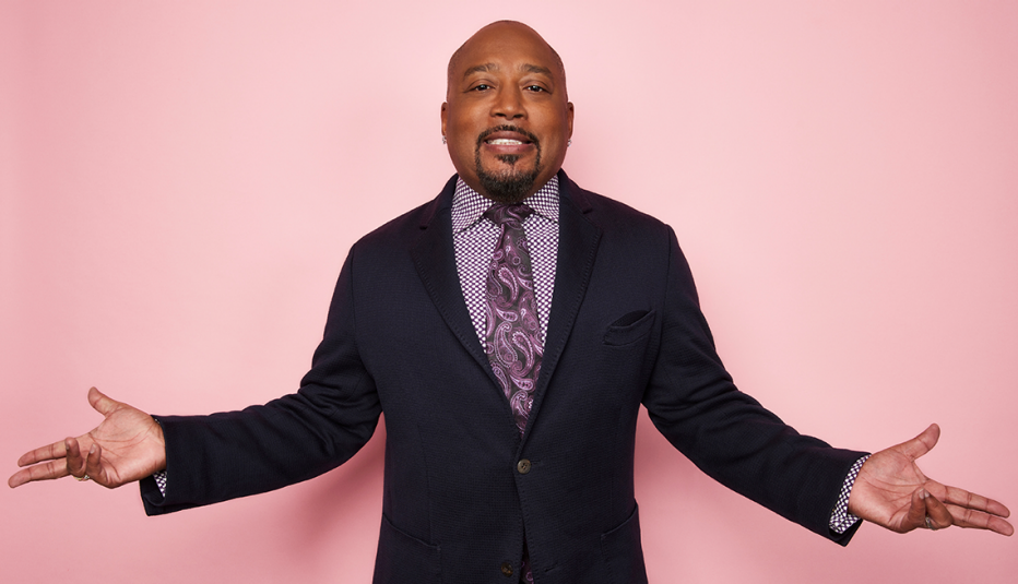 daymond john standing in business suit with hands out to both sides; pink background
