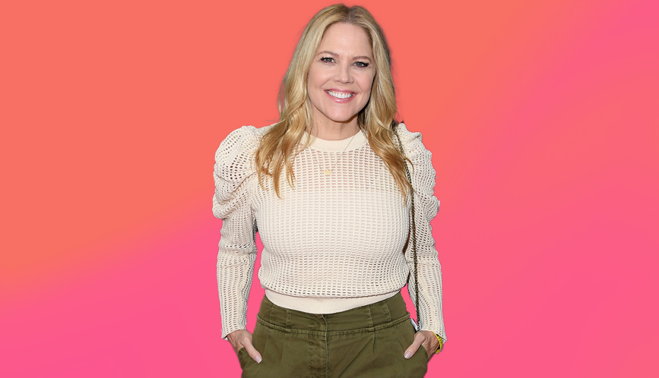 mary mccormack standing in white shirt and green pants; hands in pockets; pink background