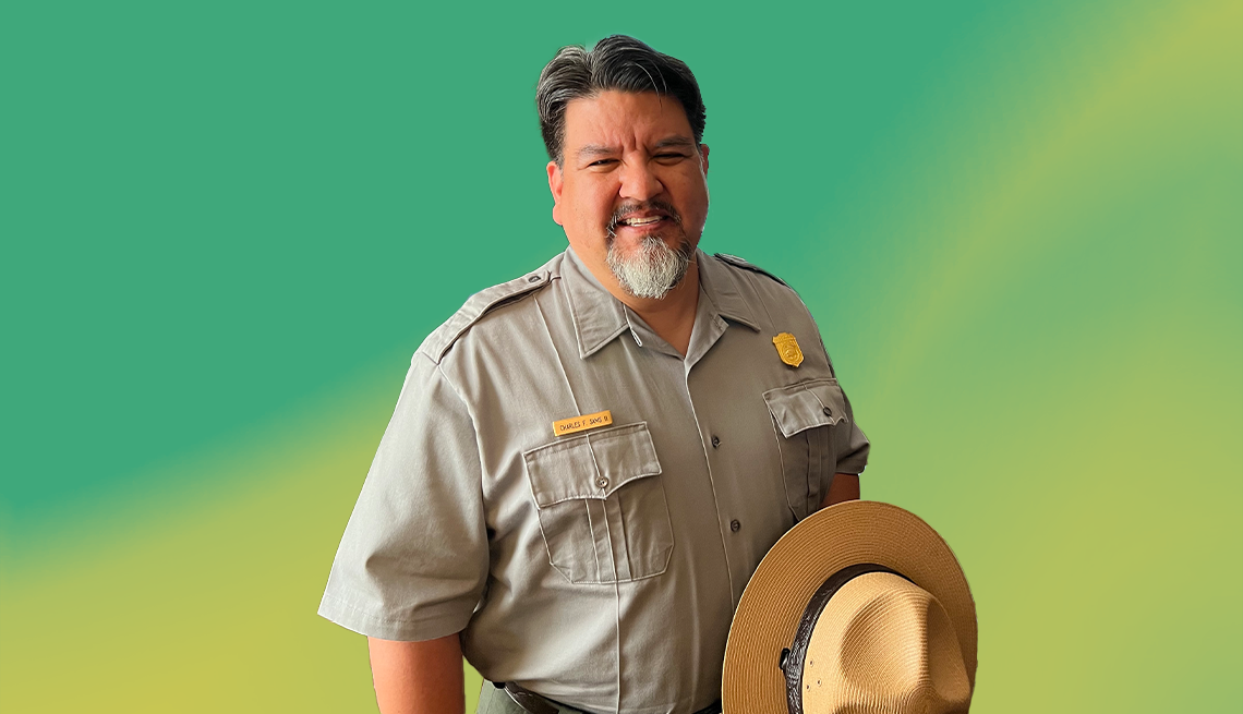 chuck sams in national park service uniform holding hat against green and yellow ombre background