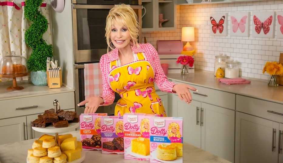 dolly parton wearing apron in kitchen with her dolly baking supplies and baked goods on table in front of her