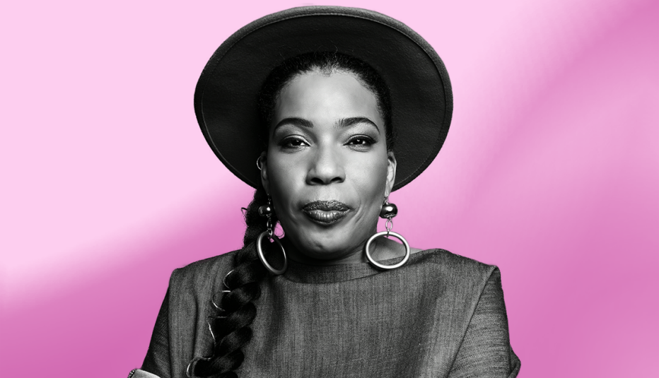 macy gray wearing hat; hair in braid lying in front of right shoulder and arm; pink ombre background