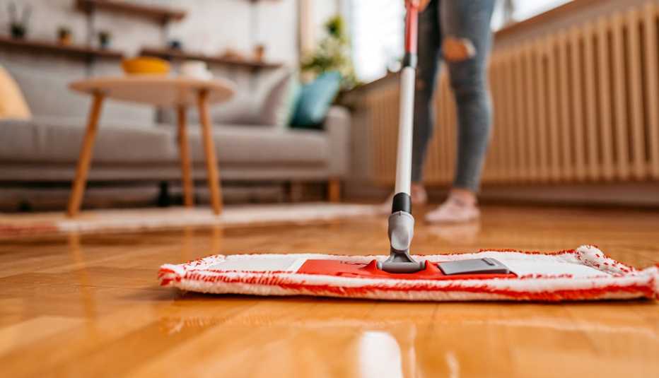 Someone cleaning hardwood floor with a flat mop; couch and table in background