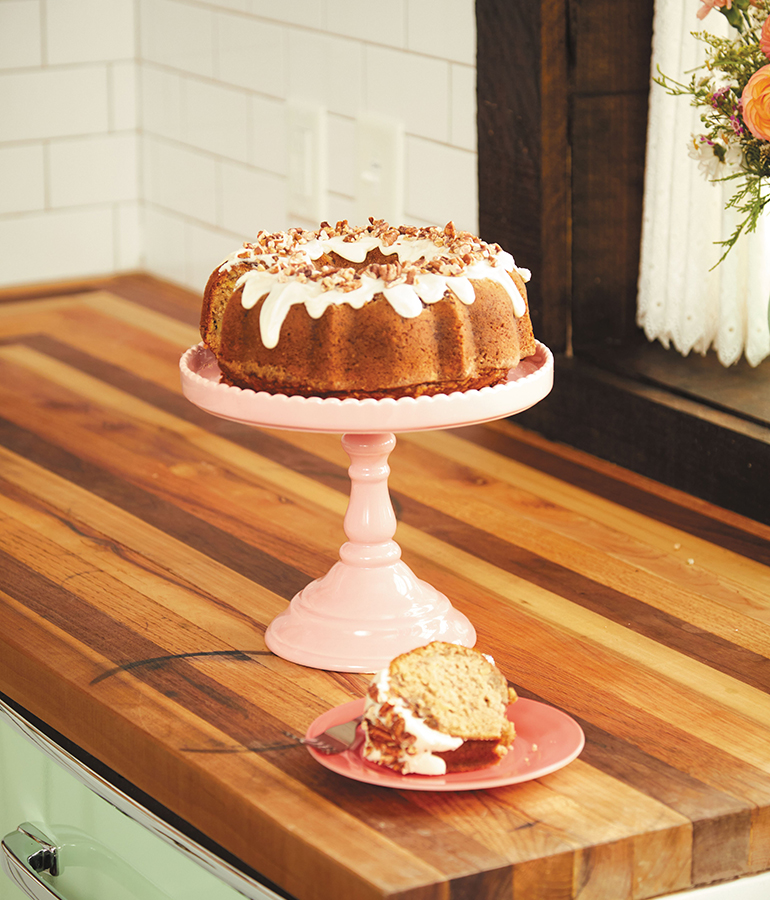 hummingbird cake on cake dish on table; piece of cake on plate beside the cake dish