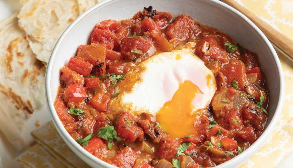 bowl of shakshuka! with a nod to india from the global pantry cookbook, showing a runny egg surrounded by cooked tomatoes and flatbread beside the bowl