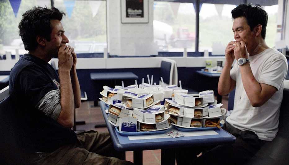 kal penn and john cho eating at table with a lot of mini burgers and drinks in a still from harold and kumar go to white castle