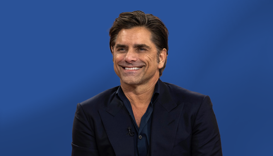 john stamos wearing black against blue ombre background